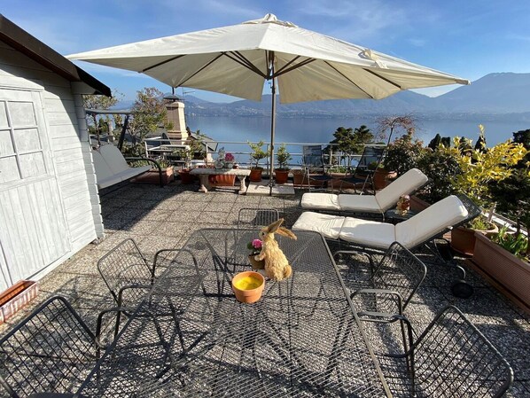 A patio with outdoor furniture, a large umbrella, and a view of a lake and mountains.