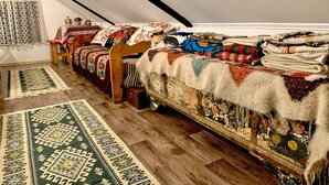 A cozy attic room with wooden floors, a sloped ceiling, and a variety of colorful blankets and rugs. - Charming Traditional House in a Pristine Location (Fundata)