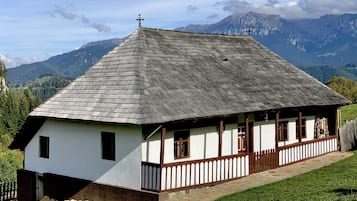 A traditional wooden house with a steeply pitched roof, a stone foundation, and a wooden fence surrounding the property.
