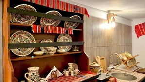 A kitchen with wooden shelves holding various ceramic dishes and a sink with a wooden drying rack. - Charming Traditional House in a Pristine Location (Fundata)