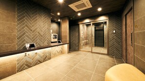 A modern bathroom with a herringbone tile pattern, a reception desk with a digital screen, and a glass elevator. - Rakuten Stay Fukuoka - Yakuin (Fukuoka)