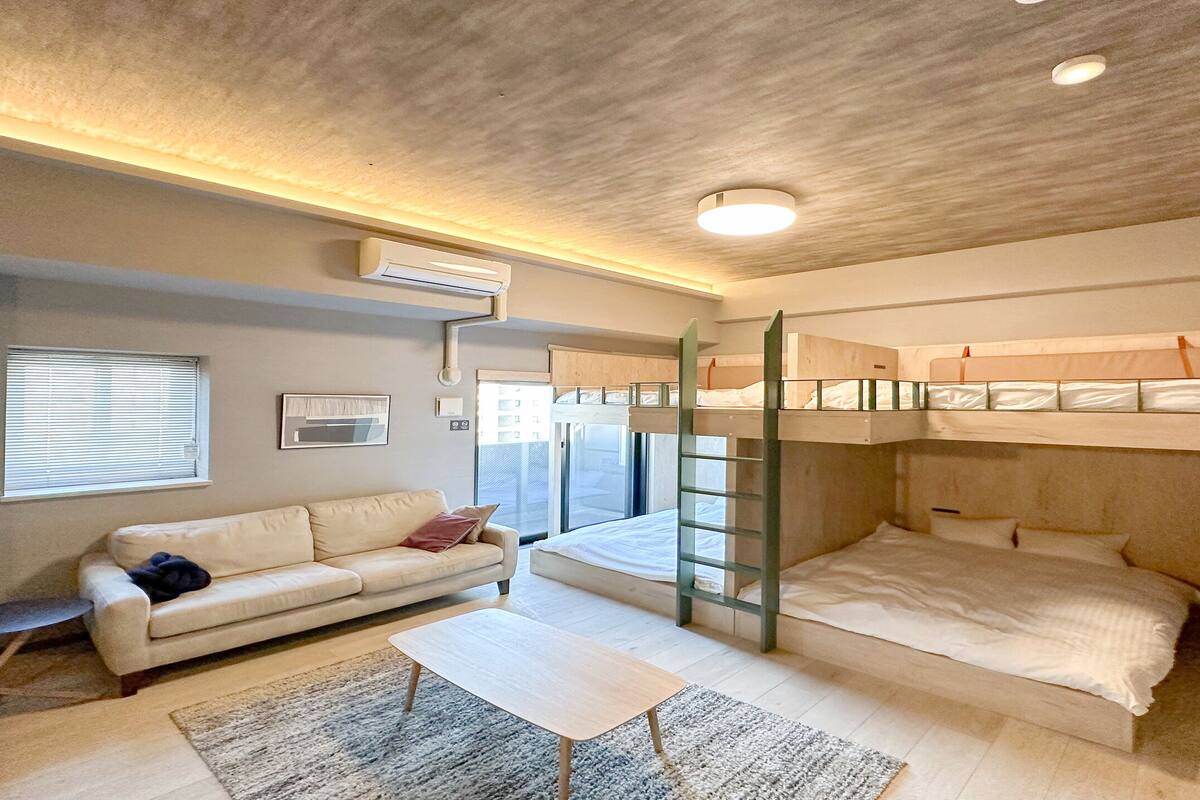 Een kleine kamer met stapelbedden, een bank, een tafeltje en een raam met luiken.