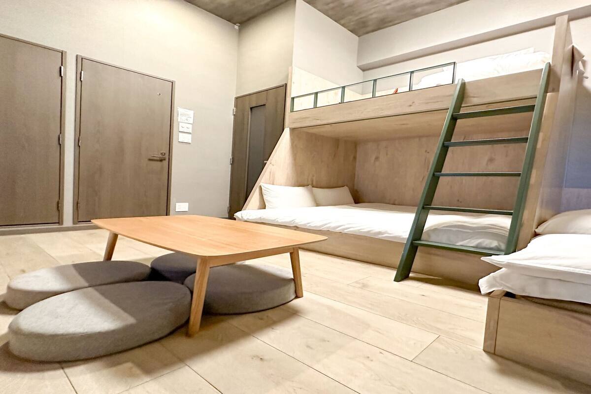Een kamer met stapelbedden, een houten tafel en een trap.