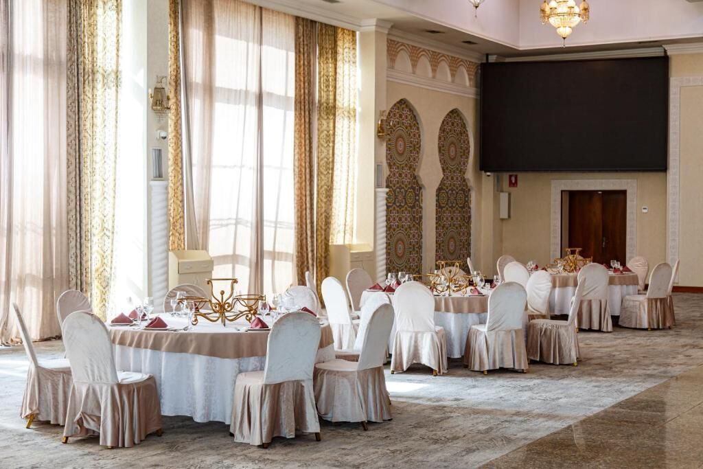 A banquet hall with round tables, white chairs, and a large screen.