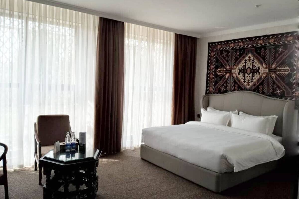 A hotel room with a large bed, a small table, a chair, and a decorative tapestry on the wall.