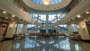 Un hall d’entrée spacieux avec un plafond haut, un lustre central et plusieurs coins salon.