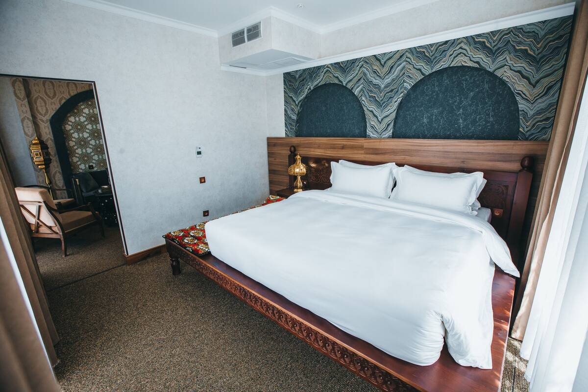 A hotel room with a large bed, a wooden headboard, a patterned wall, and a mirror.