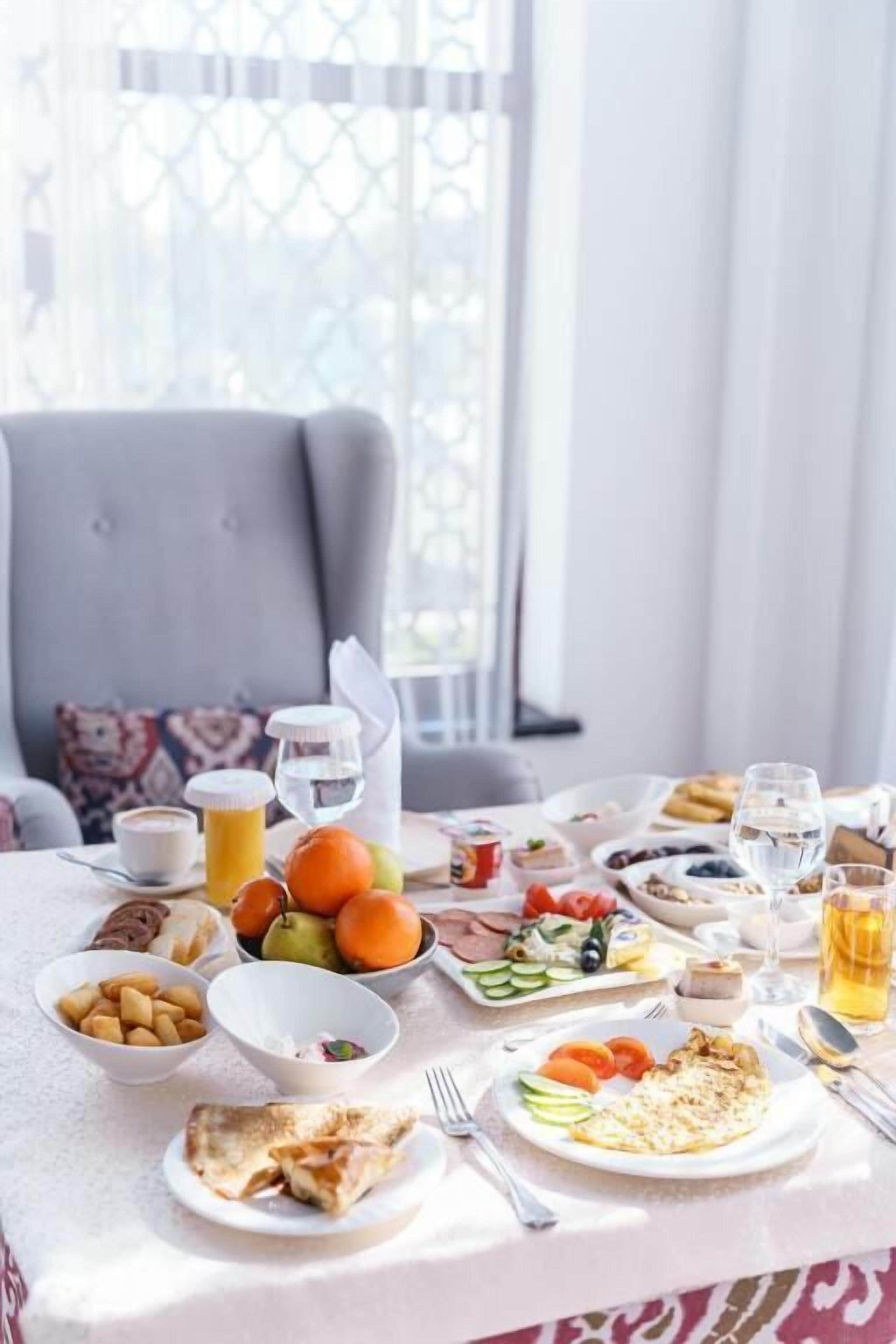 Une table de petit-déjeuner dressée avec divers plats, notamment des fruits, des œufs et des toasts, dans une pièce dotée d’une fenêtre et d’une chaise.