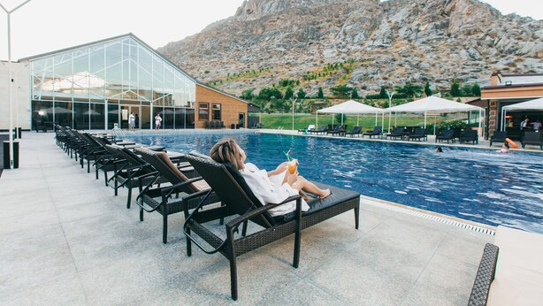 Un espace piscine avec des chaises longues, un bâtiment en verre et des montagnes en arrière-plan.