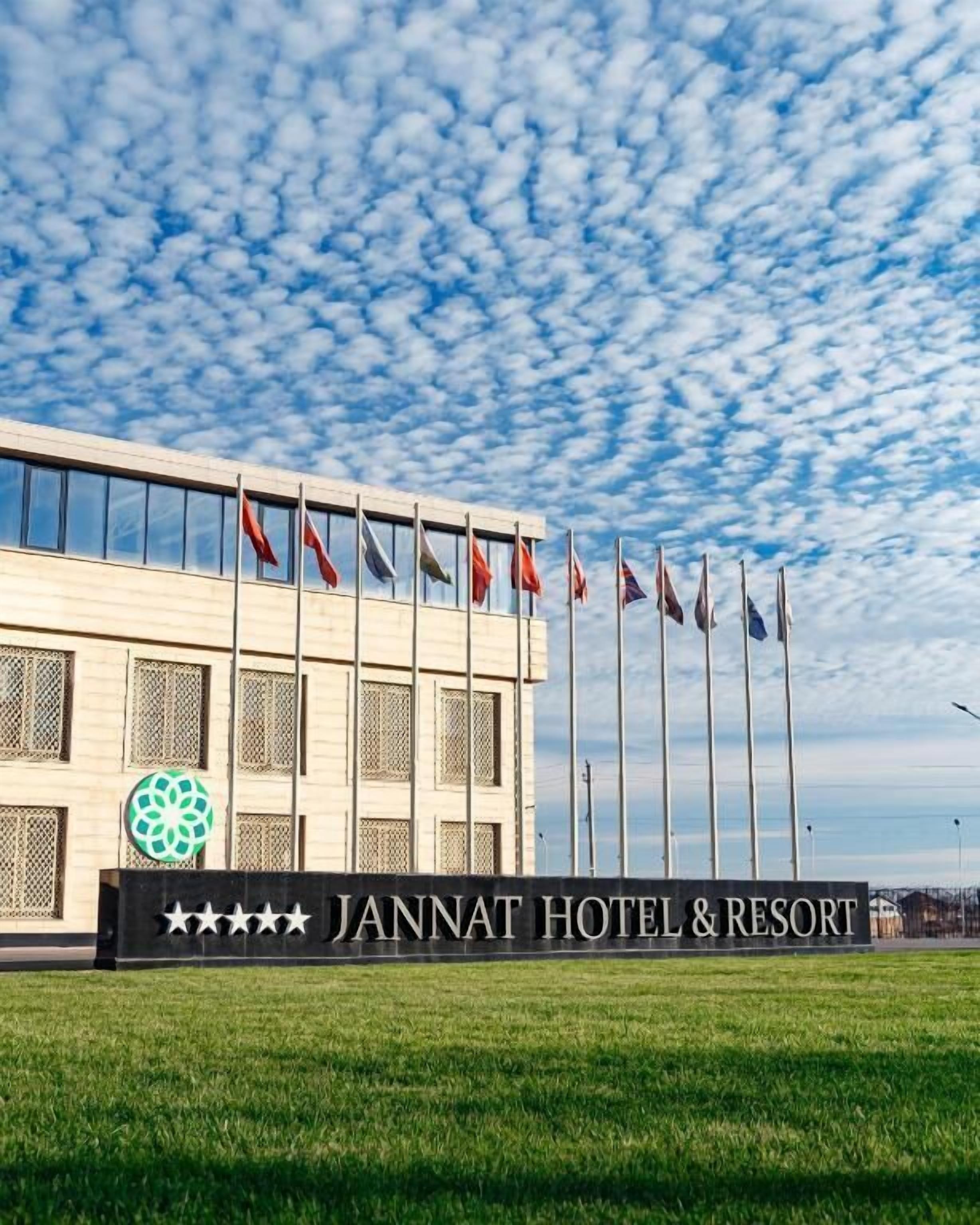 A hotel with a modern facade, a signboard with the name 'JANNAT HOTEL & RESORT', and multiple flags in front.