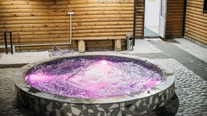 Un bain à remous aux carreaux de mosaïque, entouré d’un sol en pierre et de murs en bois.