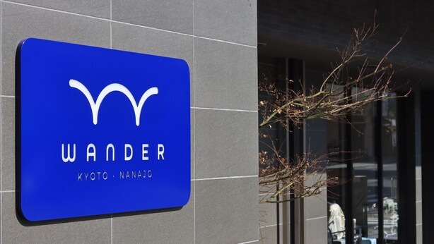 Une enseigne bleue sur laquelle on peut lire les mots « WANDER » et « PHOTO - NANAJO », fixée à la façade d’un immeuble.