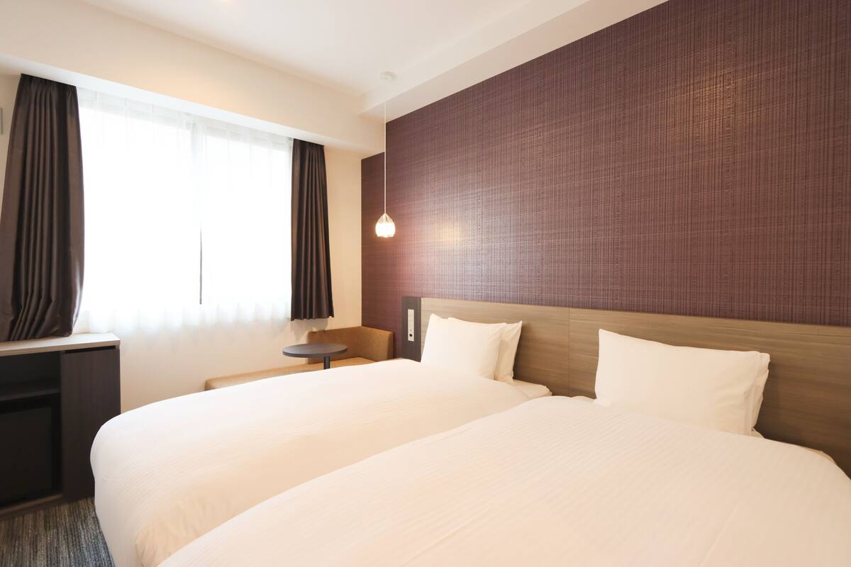 Une chambre d’hôtel avec deux lits, un bureau, une chaise et une petite table.