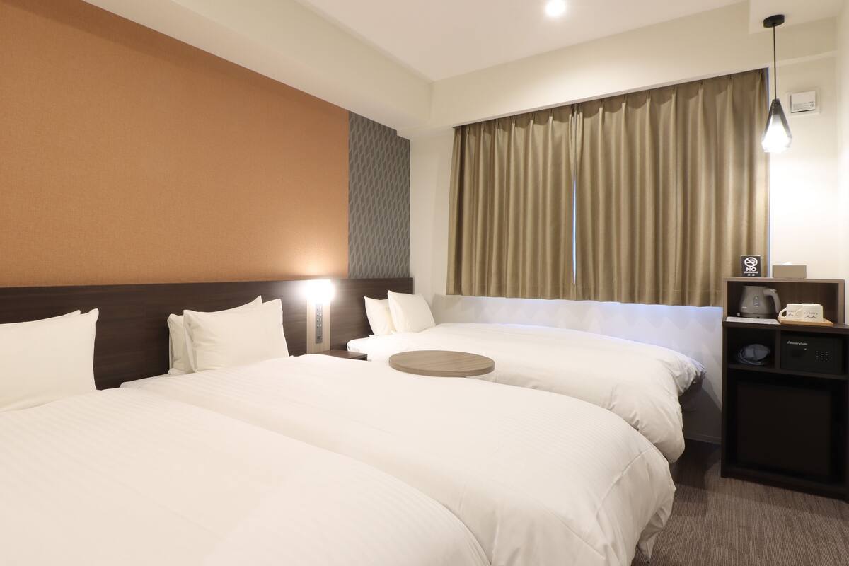 Une chambre d’hôtel avec deux lits, une table de chevet, une machine à café et une lampe.