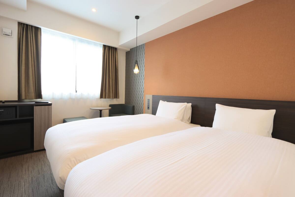 Une chambre d’hôtel avec deux grands lits, un bureau, une chaise et une fenêtre avec des rideaux.