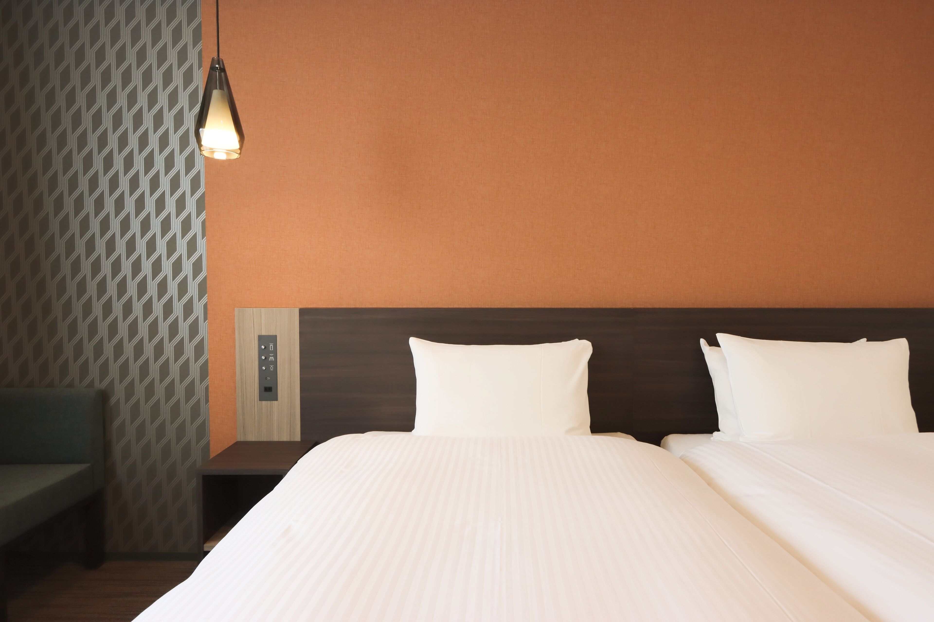 A hotel room with a bed, a nightstand, a lamp, and a patterned wall.