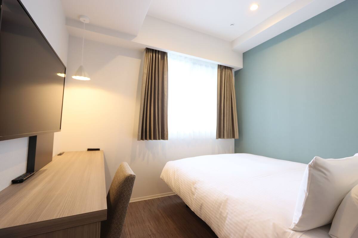 Une chambre d’hôtel avec un lit, un bureau, une chaise, une télévision et des rideaux.
