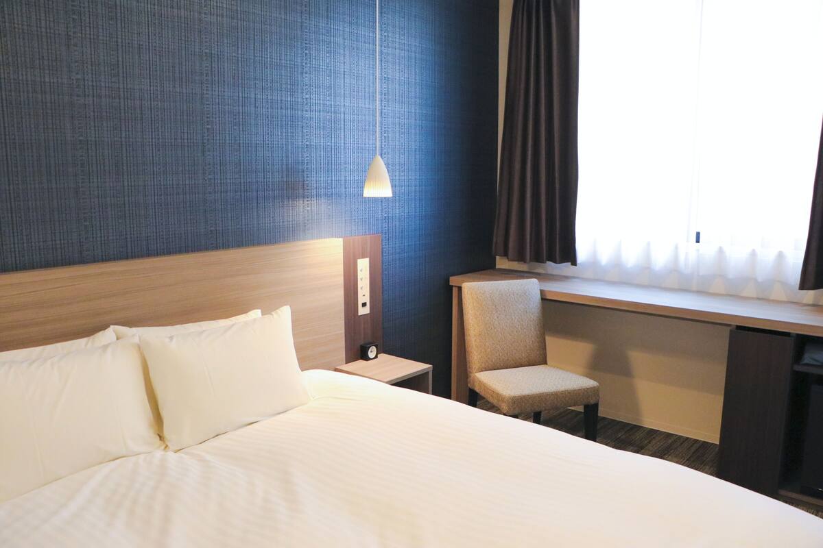 Une chambre d’hôtel avec un grand lit, un bureau, une chaise, une table de chevet et une fenêtre avec des rideaux.