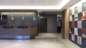 Un espace d’accueil moderne comprenant un comptoir, un téléphone et un écran numérique. Un couloir mène à une porte et un mur est recouvert de carreaux décoratifs.