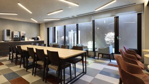 Une salle de conférence moderne équipée d’une longue table, de chaises, d’une machine à café et de grandes fenêtres avec des stores.
