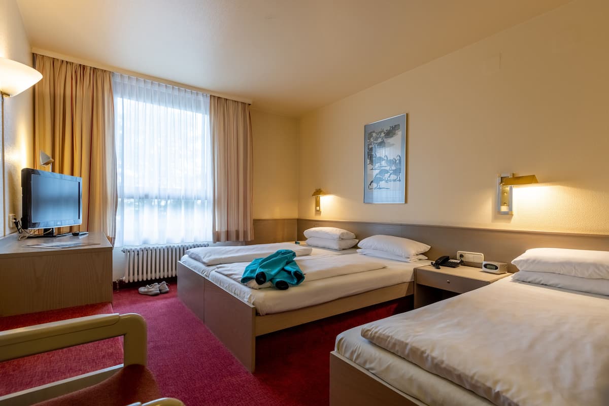 A hotel room with two beds, a desk with a computer, a chair, and a window with curtains.