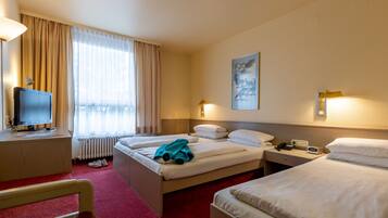 A hotel room with two beds, a desk with a computer, a chair, and a window with curtains.
