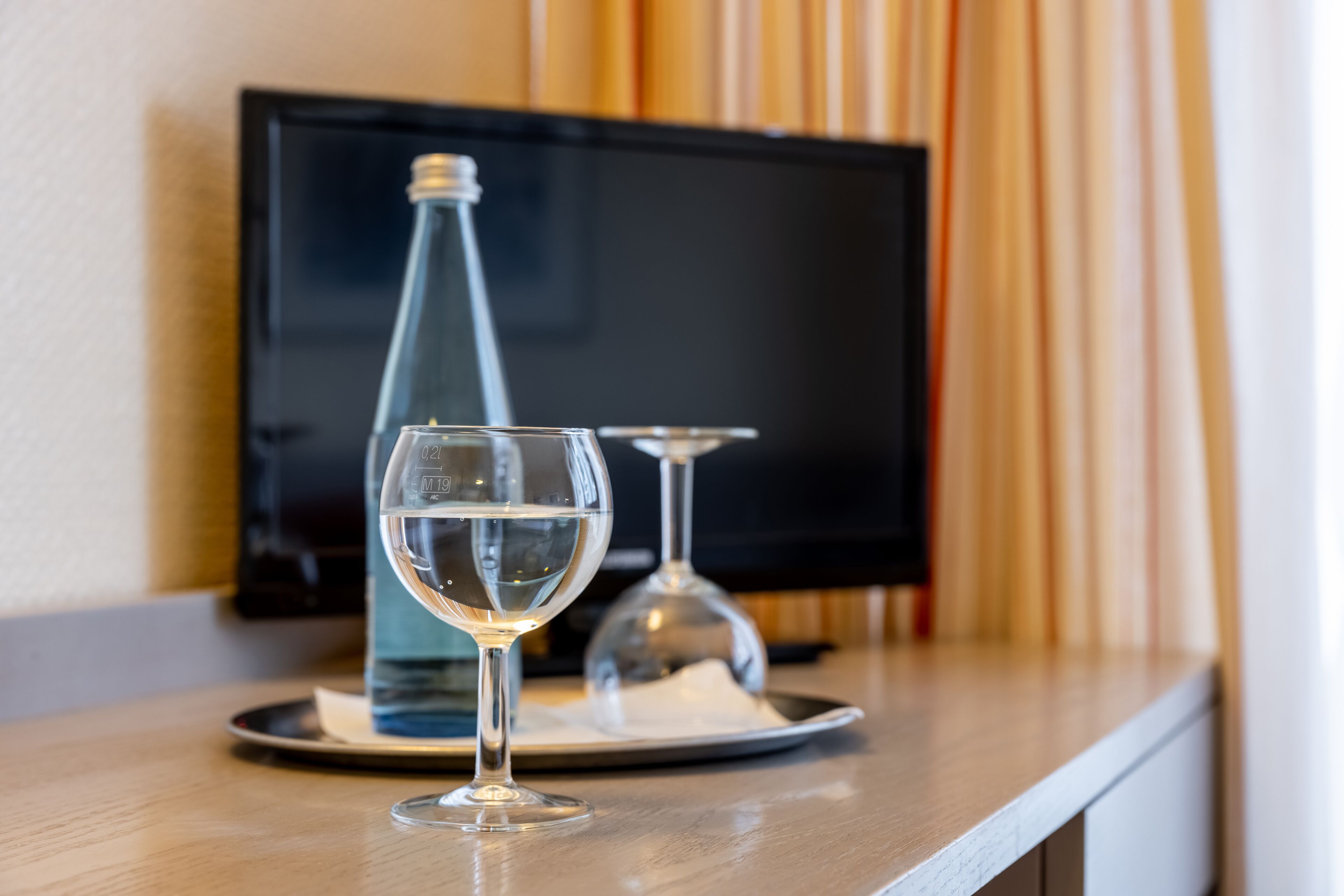 A glass of water and a bottle on a tray in front of a television.