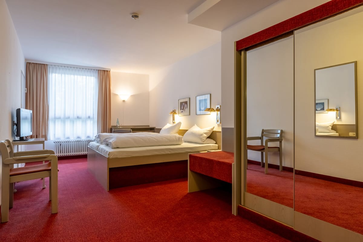 A hotel room with a bed, bedside table, chair, and a large mirror.