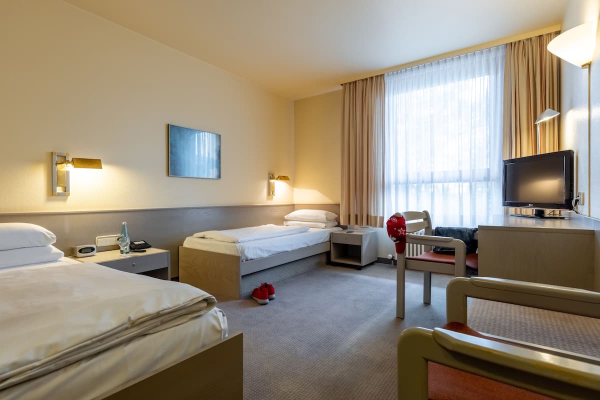 A hotel room with two beds, a desk, a chair, a television, and a window with curtains.
