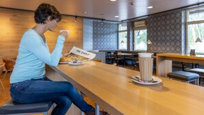 A person sitting at a wooden table in a modern cafe with a menu and a cup of coffee. - Raststättenhotel Baden-Baden (Baden-Baden)