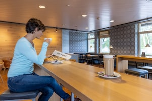 Uma pessoa sentada à mesa de madeira em um café moderno, com um menu e uma xícara de café.