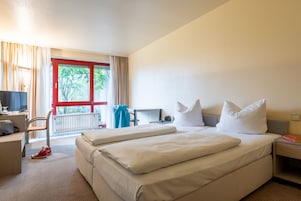 Quarto de hotel com duas camas, uma escrivaninha, uma cadeira, uma televisão e uma janela com cortinas.