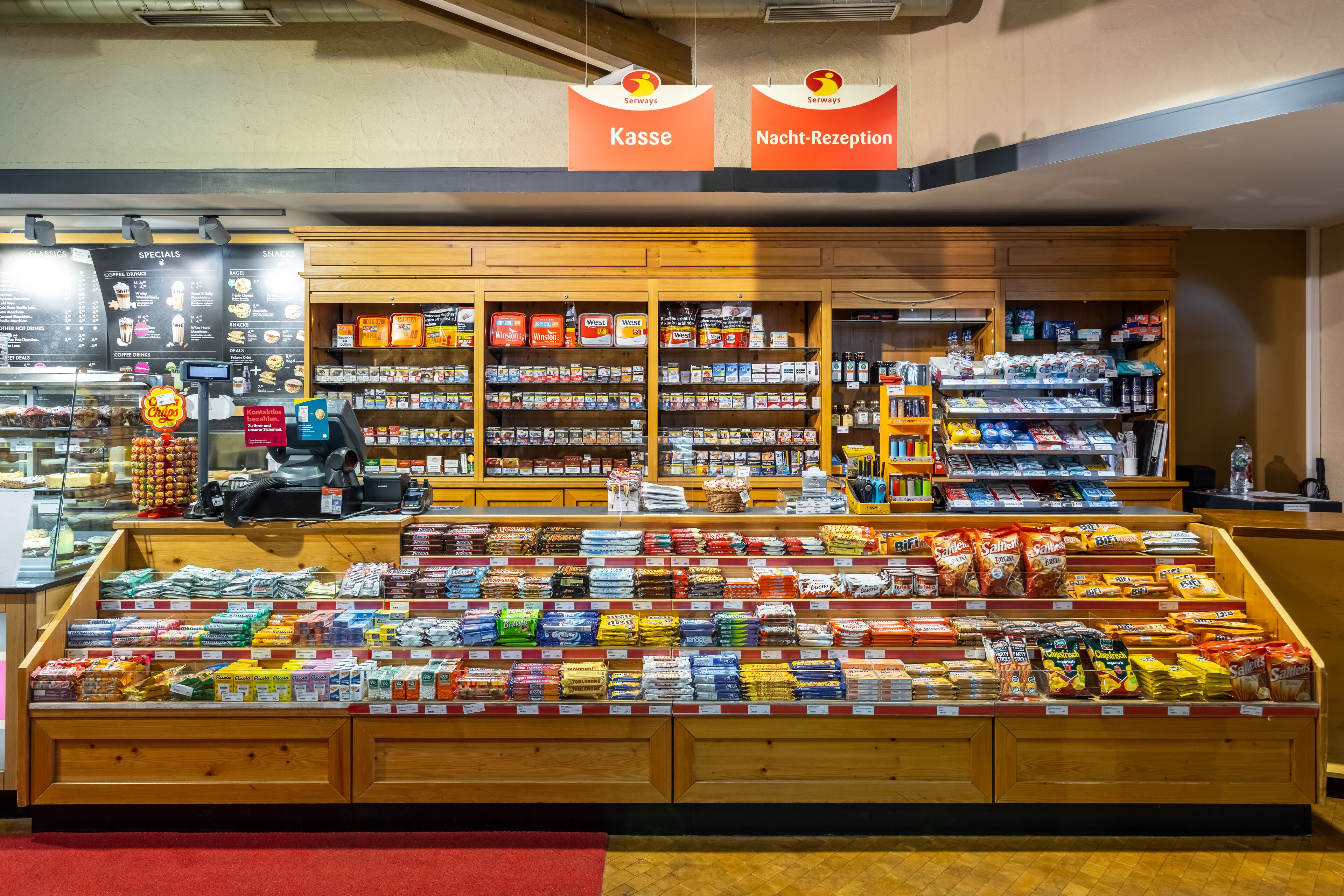 A grocery store with a deli counter, shelves stocked with snacks, and a coffee section.