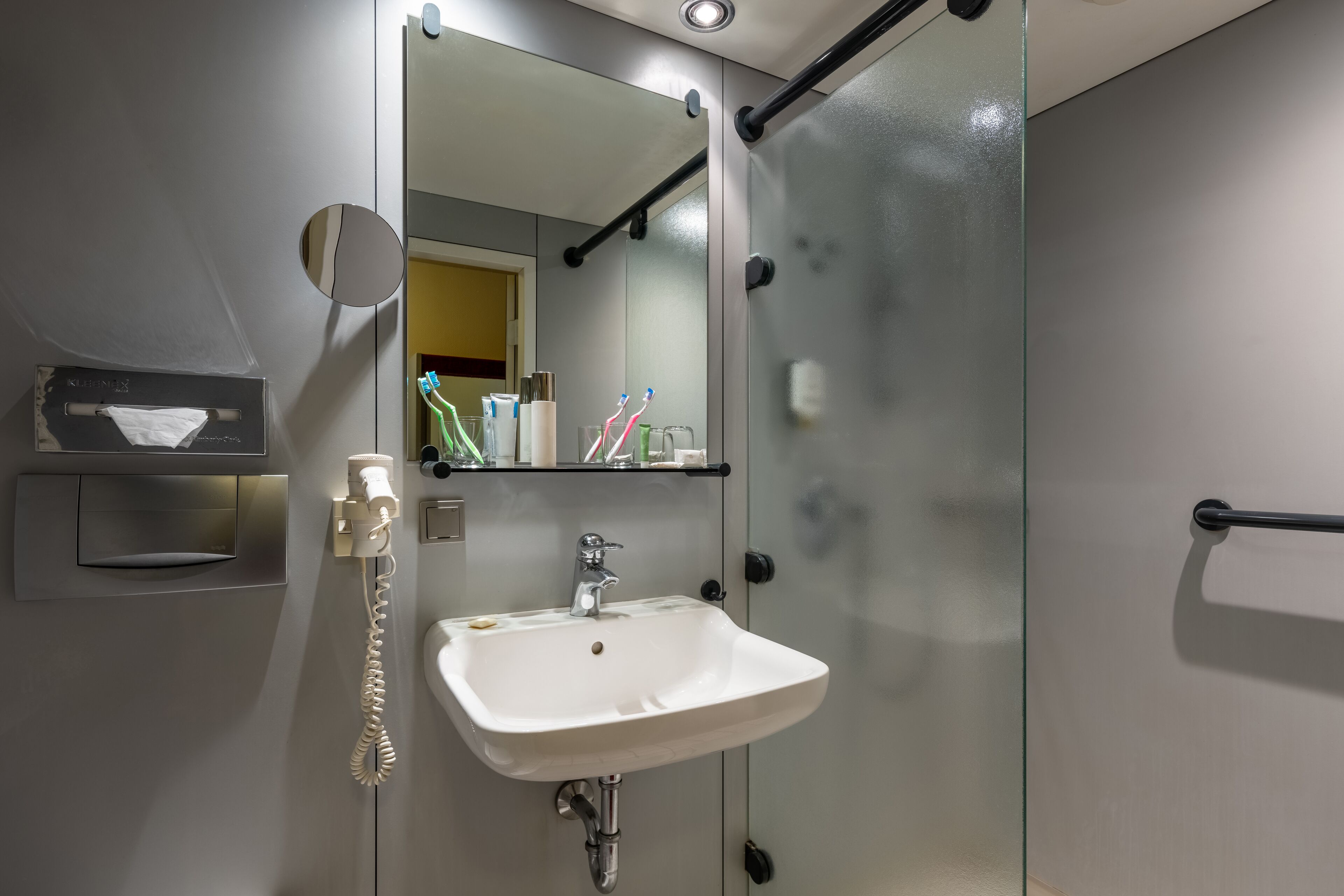 A modern bathroom with a white sink, a mirror, and a glass shower enclosure.