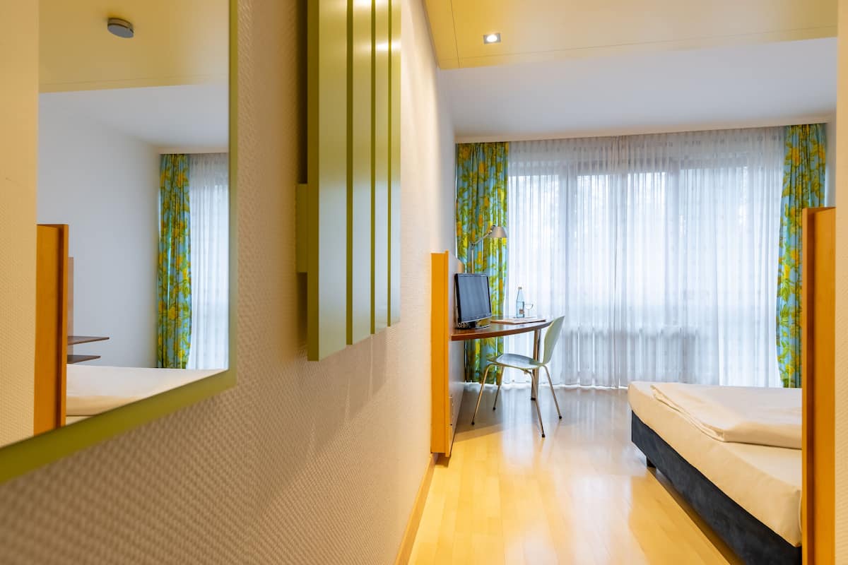 A hotel room with a bed, a desk with a chair, a television, and a window with curtains.