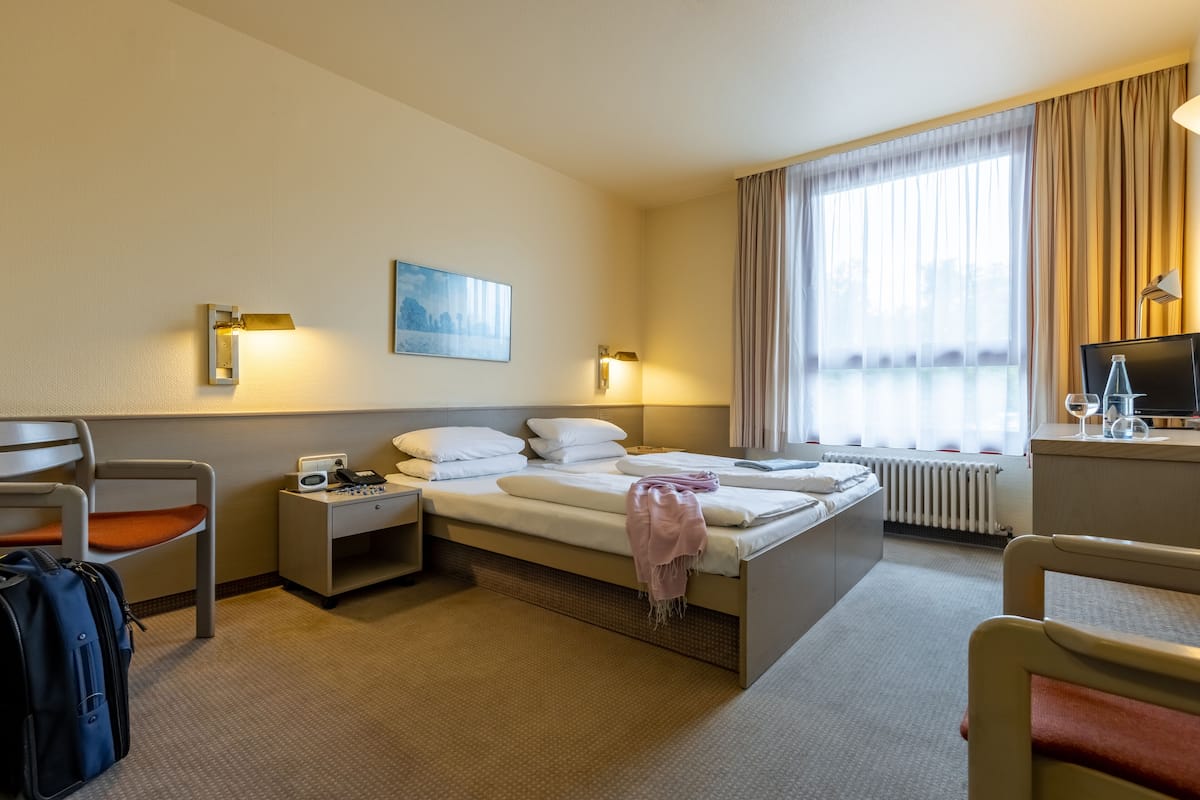A hotel room with a bed, two bedside tables, a desk, a chair, and a window with curtains.