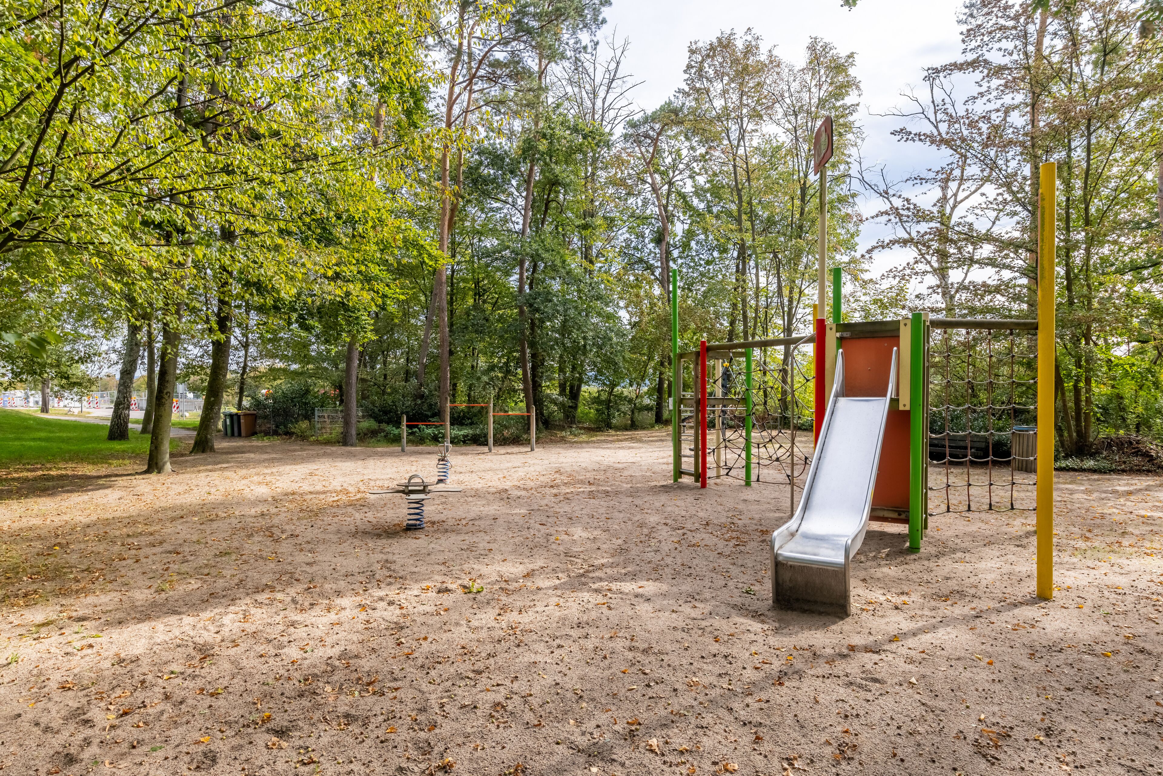 Ein Spielplatz mit Rutsche und Schaukeln, umgeben von Bäumen und einem Erdboden.