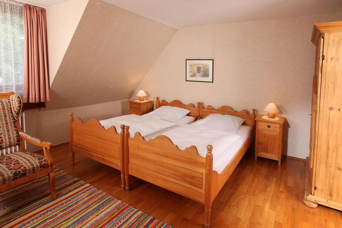 A bedroom with a wooden bed, two bedside tables with lamps, a chair, a colorful rug, and a wooden wardrobe.