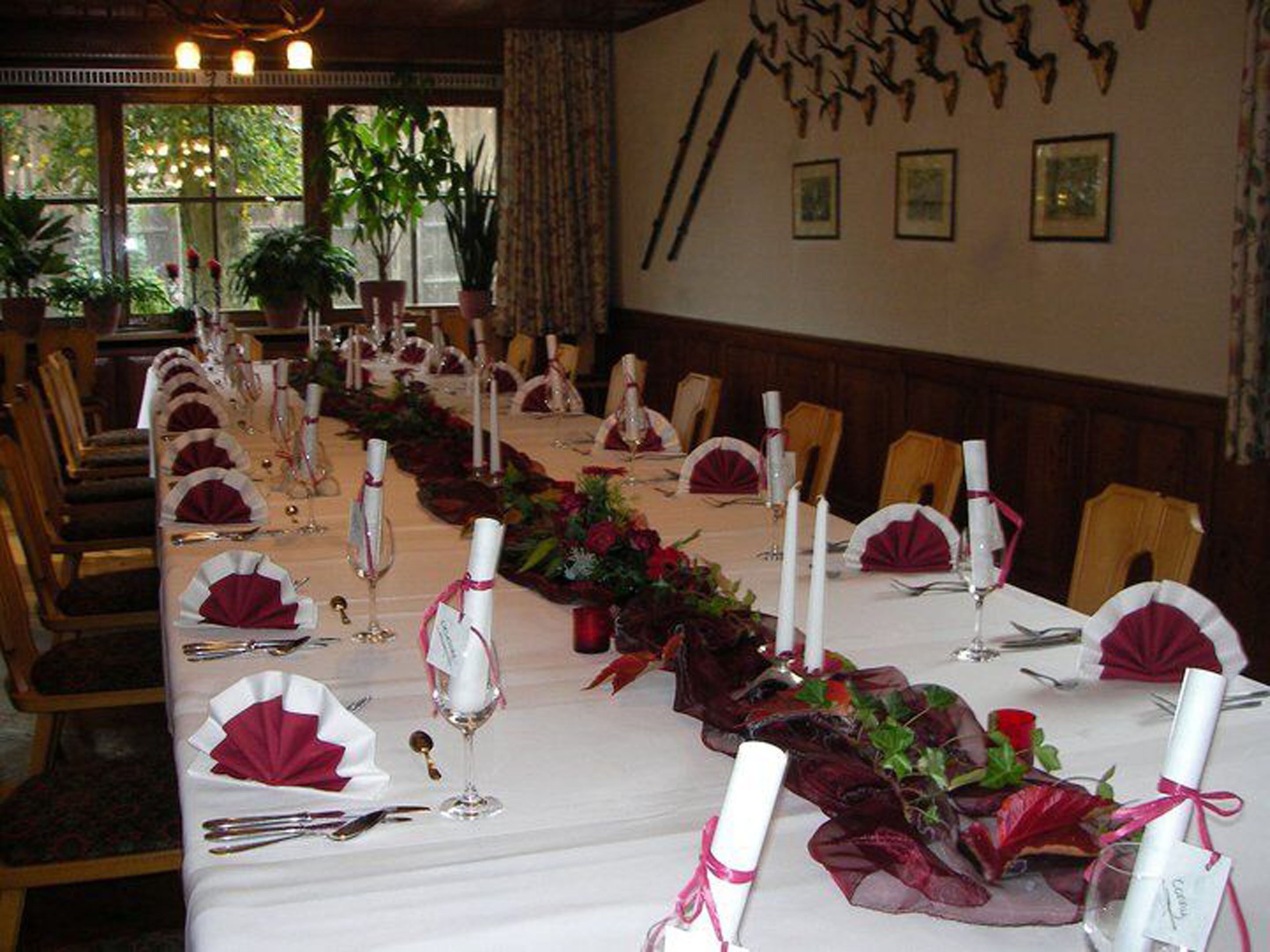 Une longue table à manger, dressée pour un événement formel, avec des nappes blanches, des serviettes rouges et des bougies.