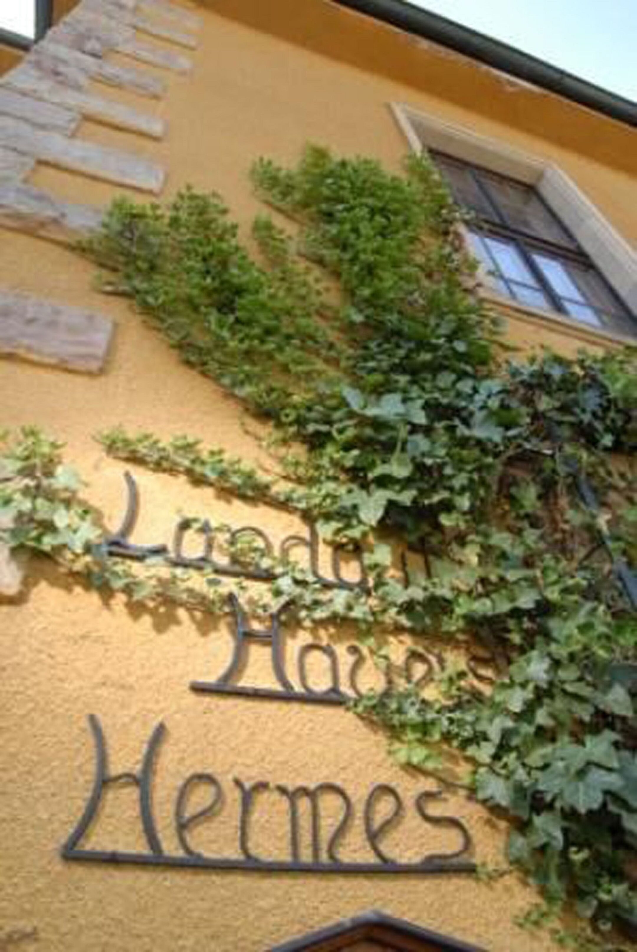 A building with a sign reading "Lodges House Hermes" partially covered by ivy.
