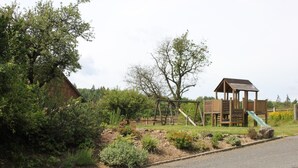 A playground with a slide and climbing structures, surrounded by a garden with various plants and a wooden playhouse. - Landgasthof Haueis (Marktleugast)