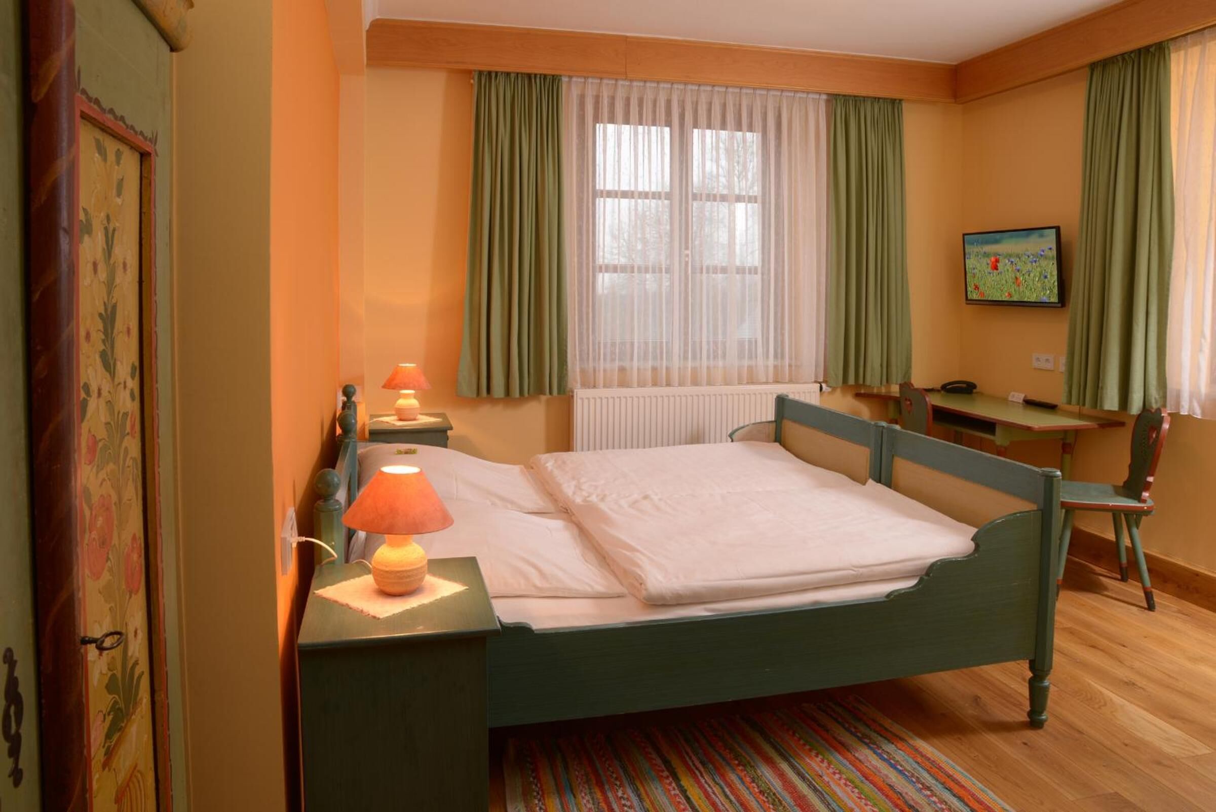 A room with a bed, a desk, a chair, a radiator, and a window with curtains.