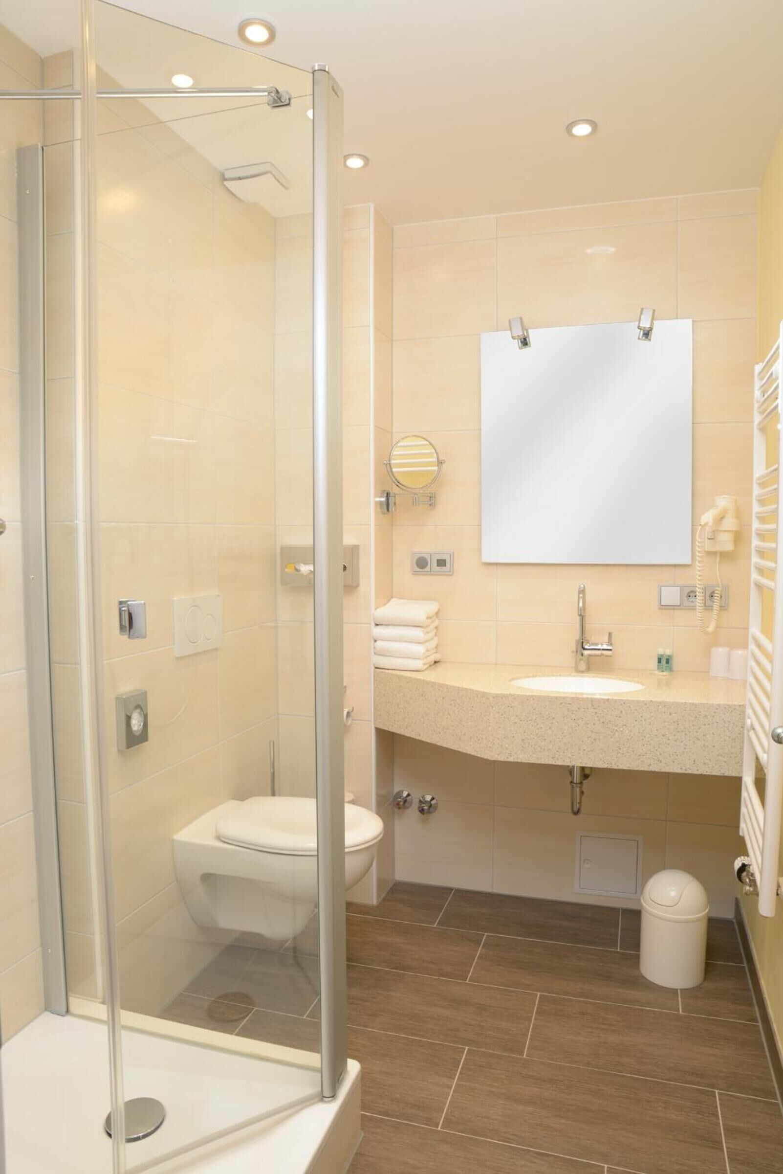 Un baño moderno con ducha envuelta en vidrio, un lavabo con espejo superior y un inodoro.