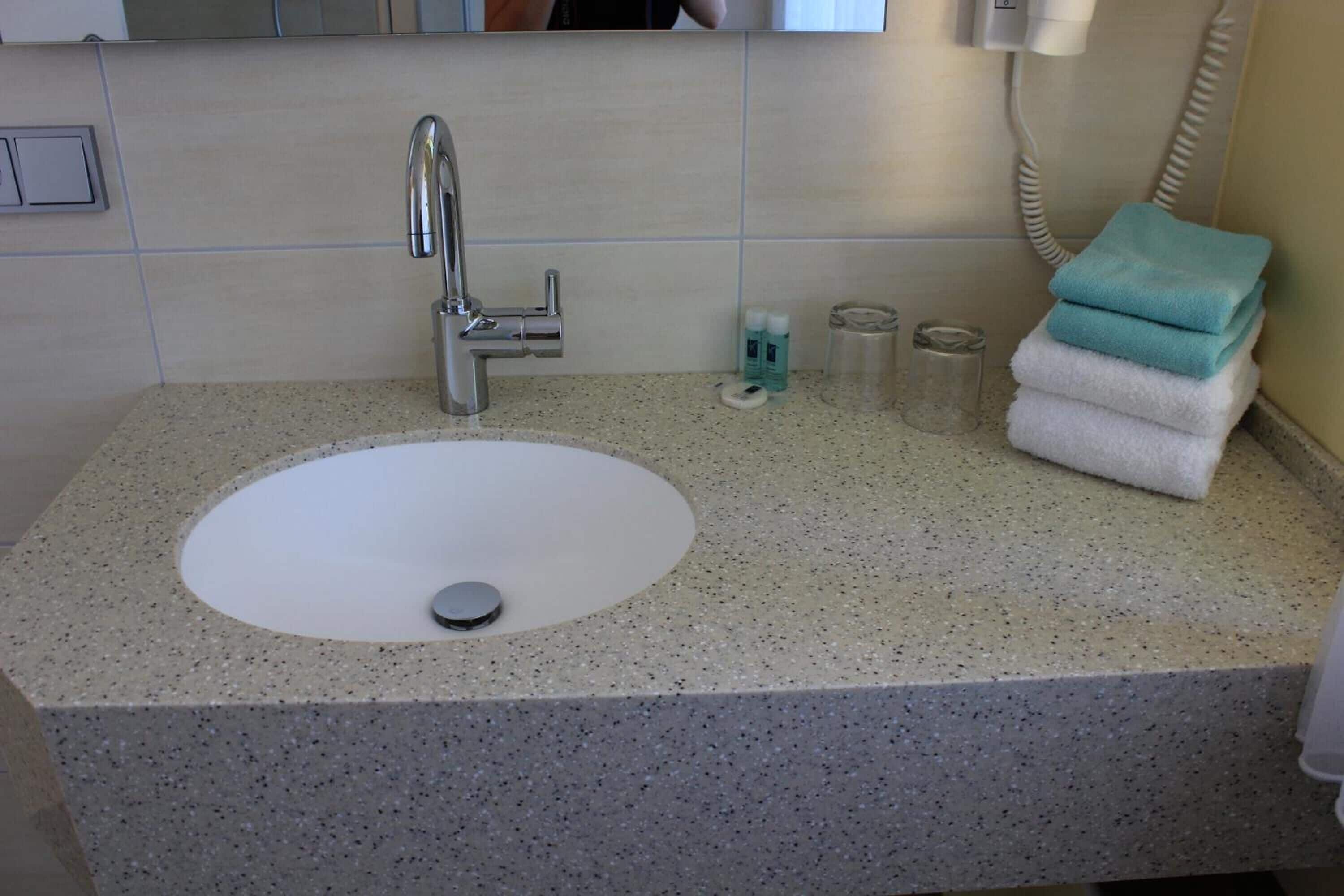 Une salle de bain avec un comptoir en granit, un lavabo blanc, un miroir et une pile de serviettes.