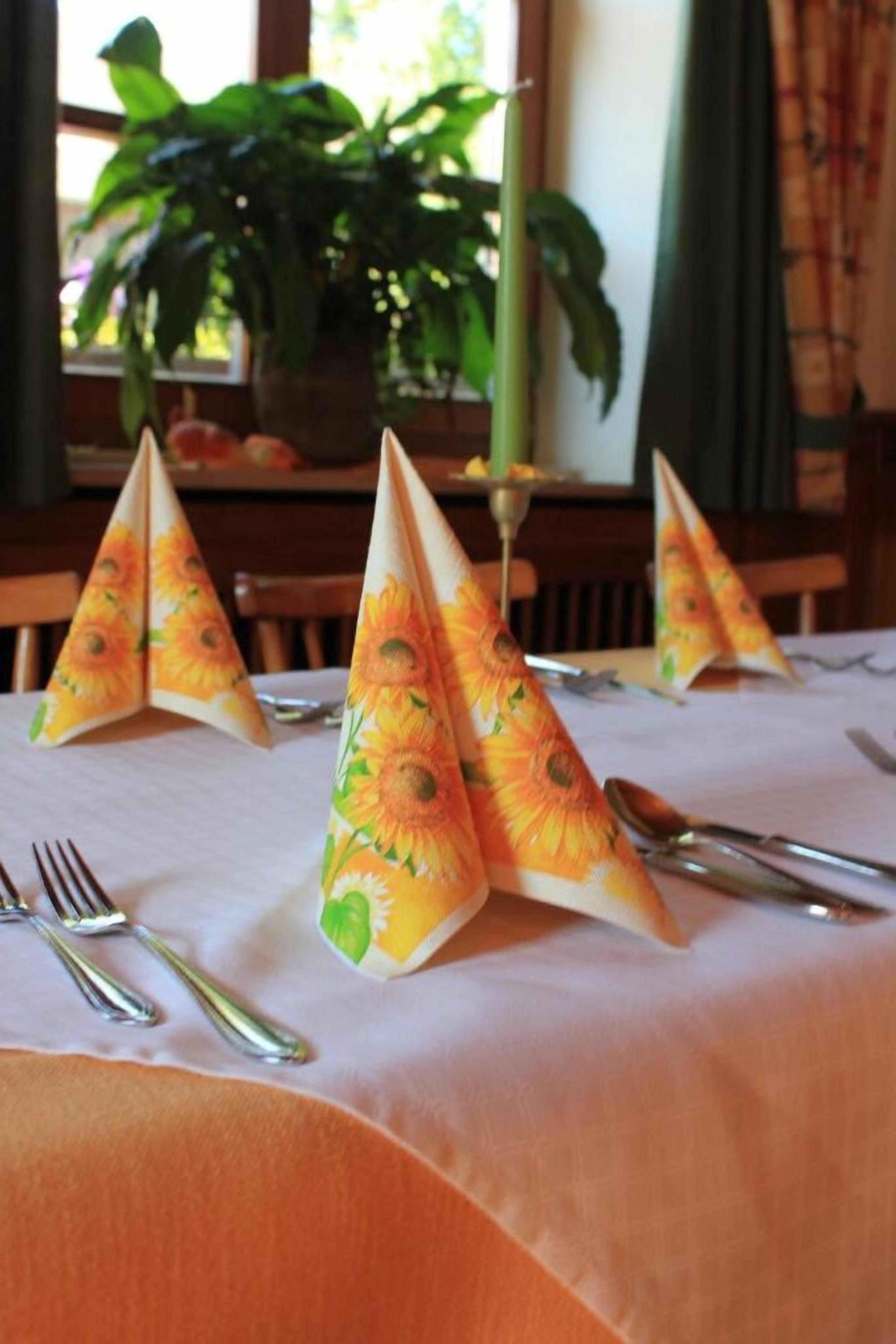 Une table dressée avec une nappe blanche, des couverts en argent et des cônes en papier ornés de motifs de tournesols.
