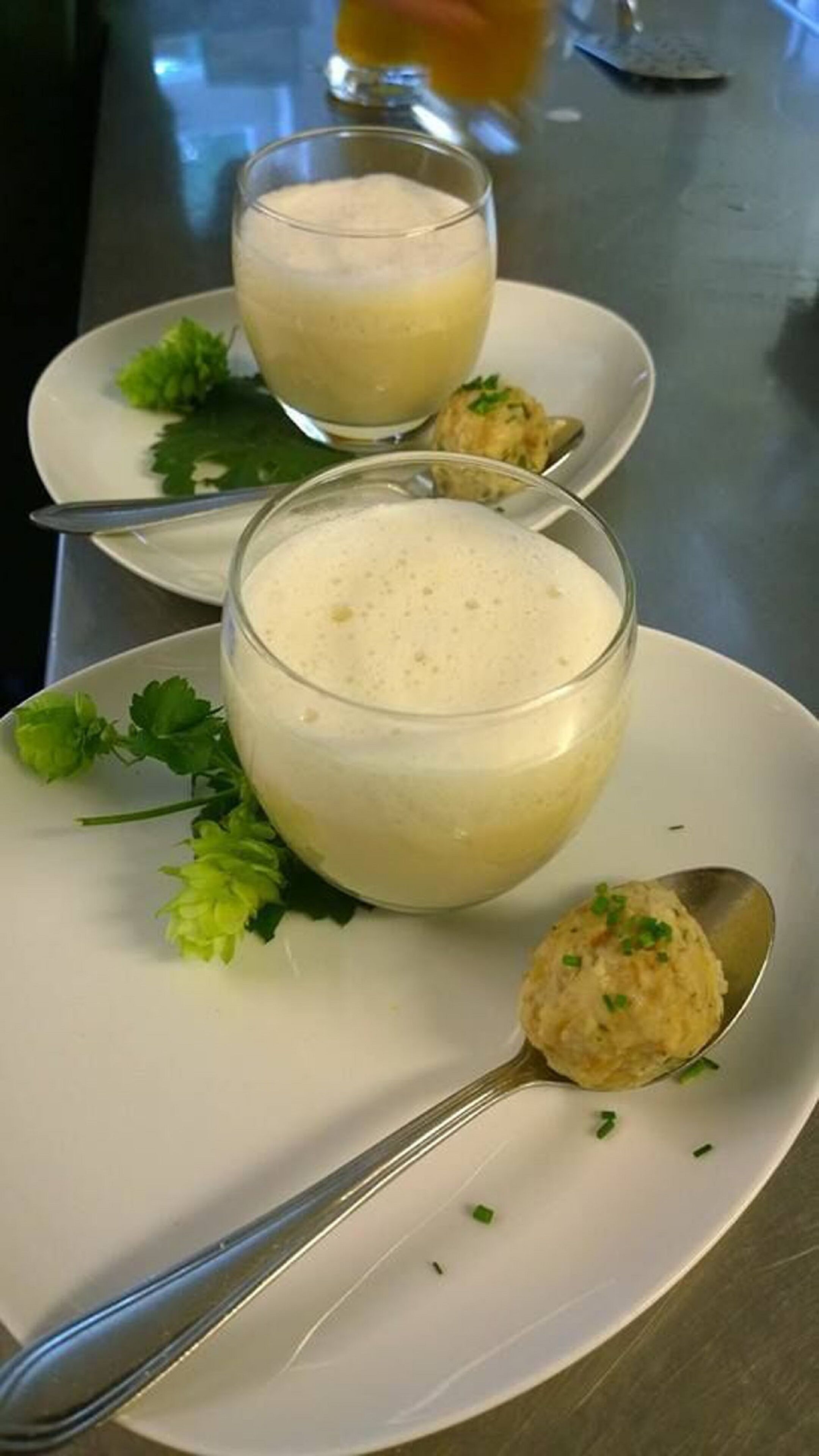 Two glasses of a creamy beverage on white plates, garnished with green herbs, with a spoon on one plate.