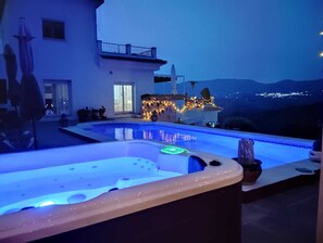 Un área de piscina moderna con un jacuzzi, una terraza bien iluminada y vistas a una cordillera.