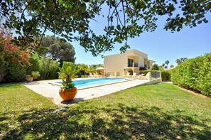 A modern house with a swimming pool, surrounded by well-maintained lawns and various plants.