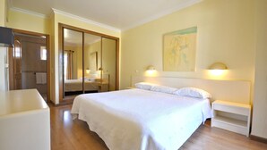 Una camera da letto con un grande letto, un armadio, un comodino e una lampada a parete.