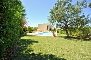 A house with a swimming pool, surrounded by a well-maintained lawn and trees.